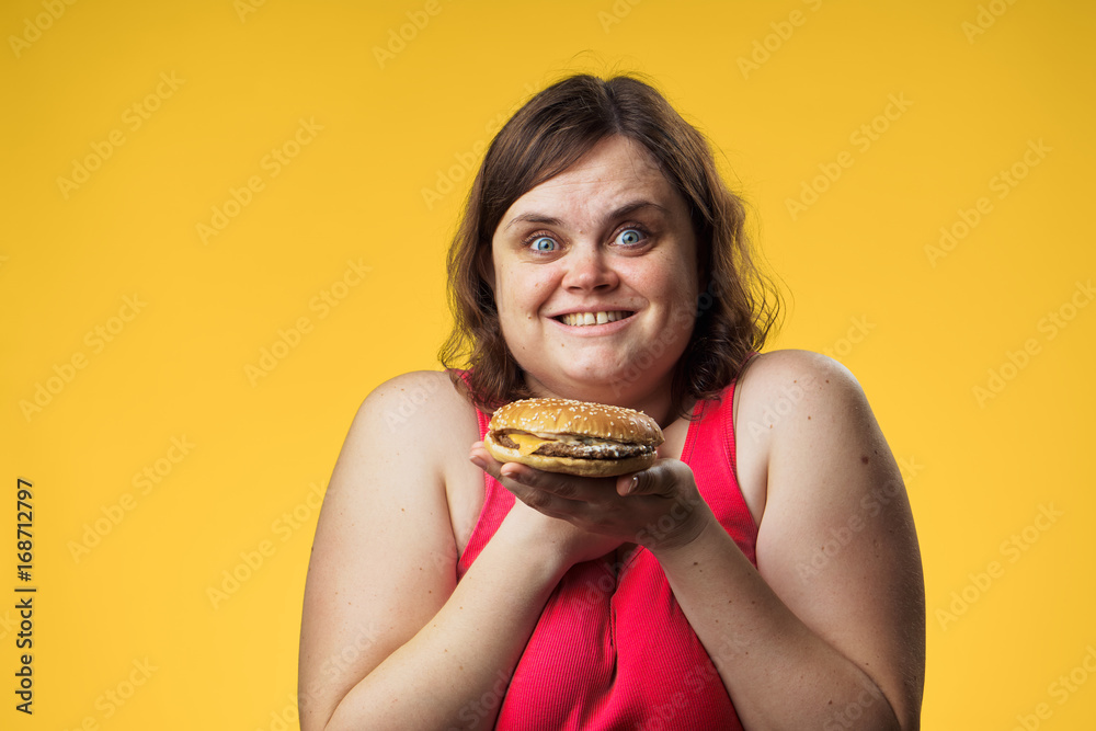 Fat woman on a yellow background holds a hamburger, fast food Fat woman on a yellow background holds a hamburger, fast food