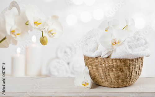 Wicker basket with spa towels on table over abstract background