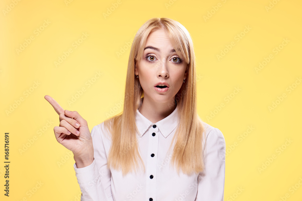Beautiful young woman on a yellow background shows up on an empty space