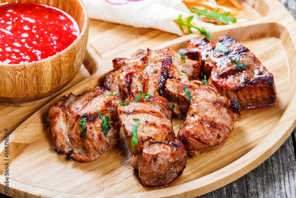 Grilled pork and vegetables with fresh salad and bbq sauce on cutting board on wooden background close up. Hot Meat Dishes. Top view