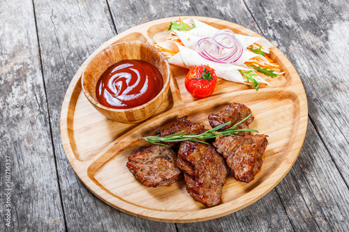 Grilled beef and vegetables with fresh salad and bbq sauce on cutting board on wooden background close up. Hot Meat Dishes. Top view