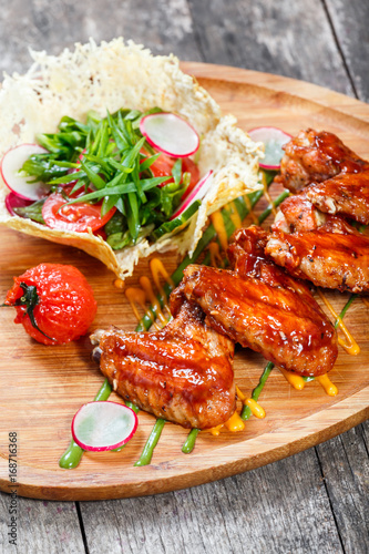 Fried chicken wings with fresh salad, grilled vegetables and bbq sauce on cutting board on wooden background close up. Hot Meat Dishes. Top view