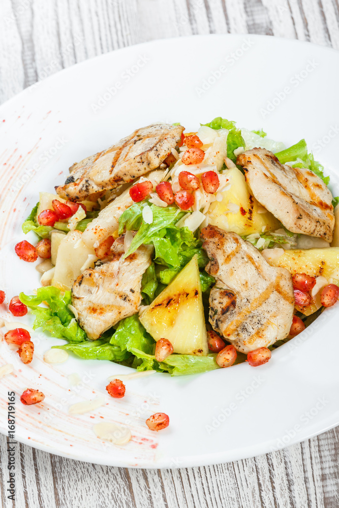 Fresh salad with chicken breast, melon, pineapples, pomegranate seeds, lettuce leaves and almond on plate on wooden background close up. Top view Fresh salad with chicken breast, melon, pineapples, pomegranate seeds, lettuce leaves and almond on plate on wooden background close up. Top view