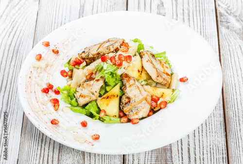 Fresh salad with chicken breast, melon, pineapples, pomegranate seeds, lettuce leaves and almond on plate on wooden background close up. Top view