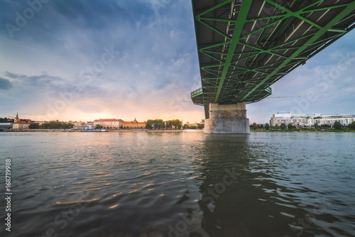 By the River under the Bridge. Skyline of Bratislava, Slovakia at Sunset in Background.
