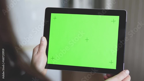 Woman wear in black sweater is holding a tablet pc with green screen and markers, making pick gestures on touchpad, defocused background, 4K