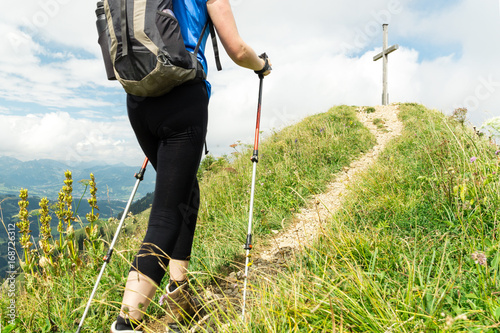 Woman running on narrow mountain trail with hiking poles.