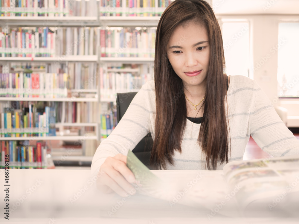 A beautiful asian woman reading a magazine in library. A beautiful asian woman reading a magazine in library.