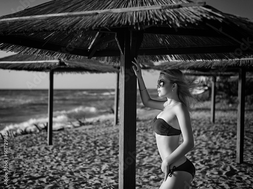 Beautiful girl on vacation on the beach near the sea, hiding from the sun under an umbrella (black and white)