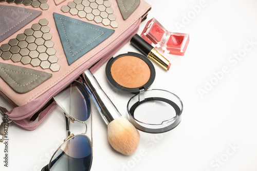 Fashionable pink woman's decorated bag with mineral powder, lip gloss, sunglasses and eyeshadow palette. Copyspace