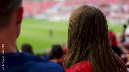 Closeup Of 2 Sports Fans Pointing To Professional Soccer Players On Field, Teen Girl Looks Excited/Surprised, She Points Again, Turns And Smiles At Camera (Slow Motion)