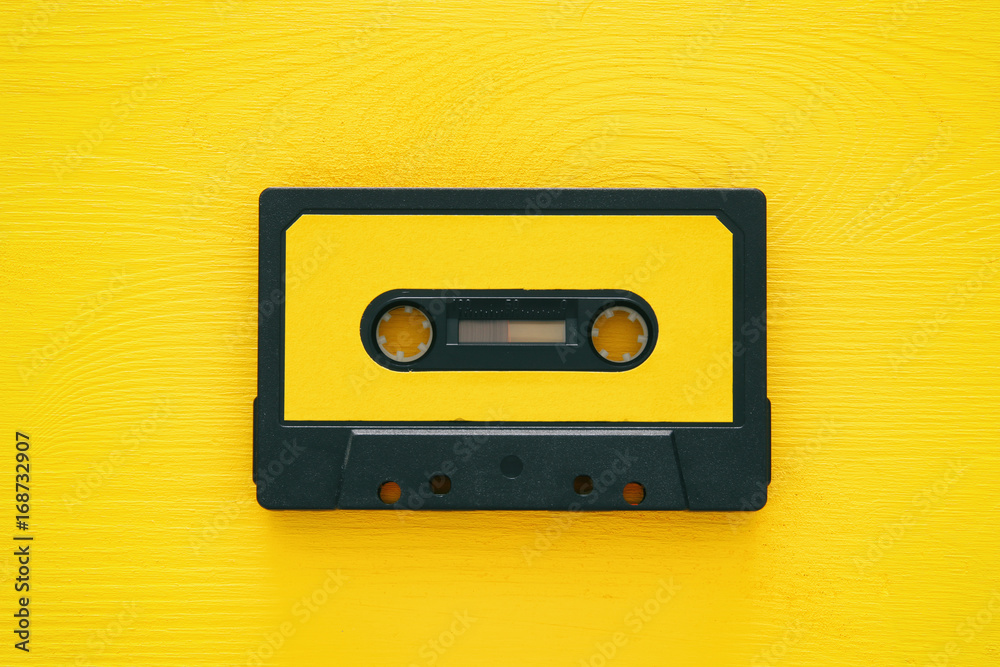 Obraz premium Retro cassette tape over yellow wooden table. top view.
