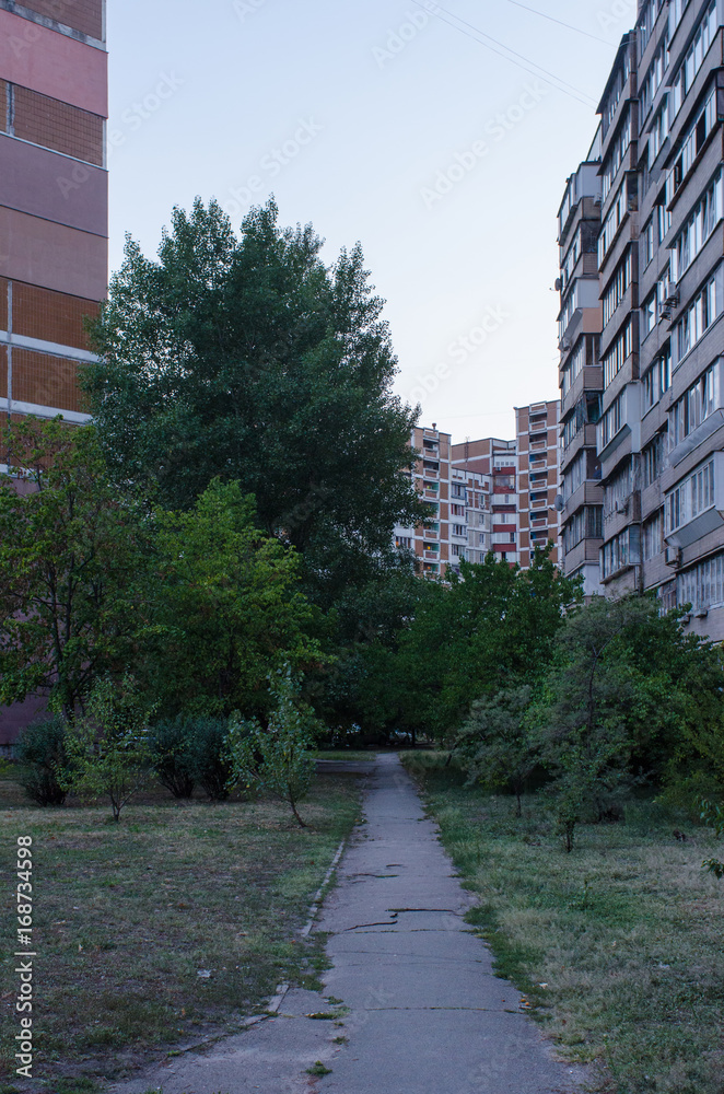 small path leading up to an old soviet era residential buildings framing the trees below them in Kiev, Ukraine, during the blue hour in summer