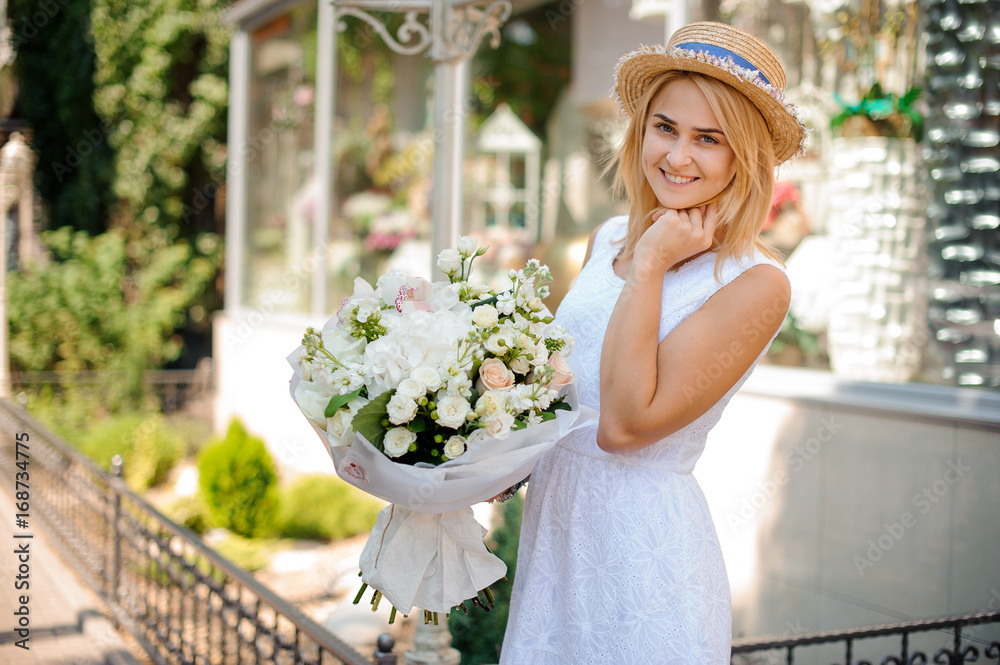 Girl in a white dress and a straw hat holds a festive bouquet