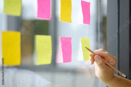 Hand point sticky note reminder on glass windows in business office.