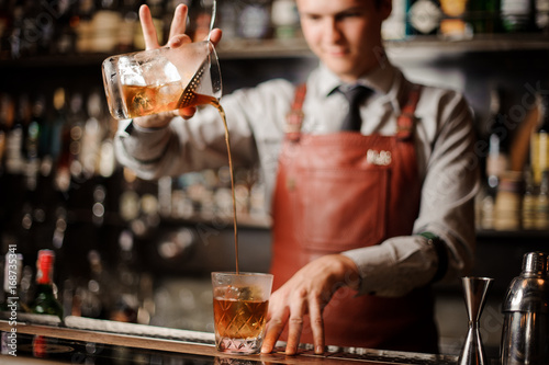 Barman in bar interior making alcohol cocktail.