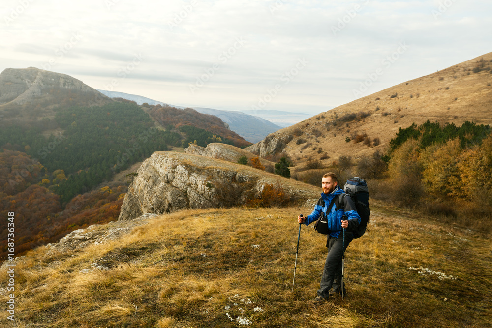 Redhead bearded hiker going up the trail path enjoying landscape. Backpacker man climbing a mountans with trekking poles. Beautiful autumn scenery