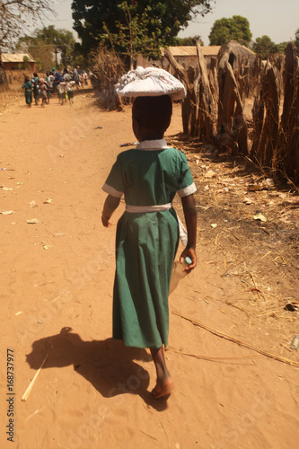 african girl in a school uniform carrying books on her head