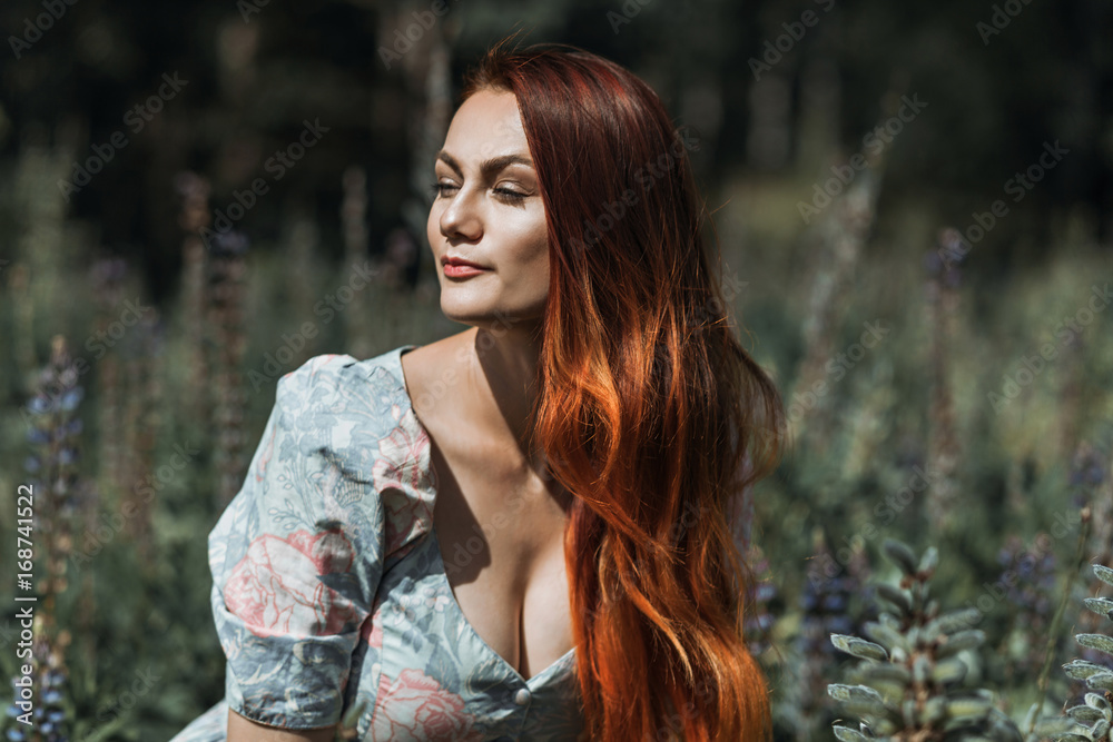 Naklejka premium Portrait of a beautiful red-haired girl in a flower field