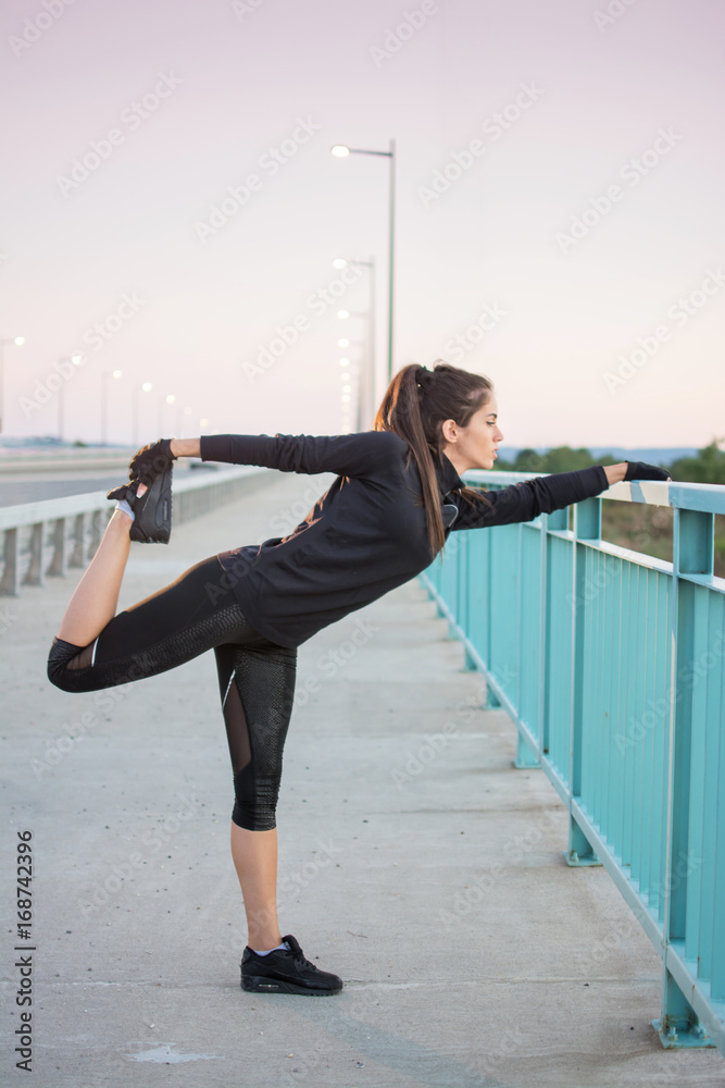 Fitness girl in sports clothing doing stretching exercises near bridge