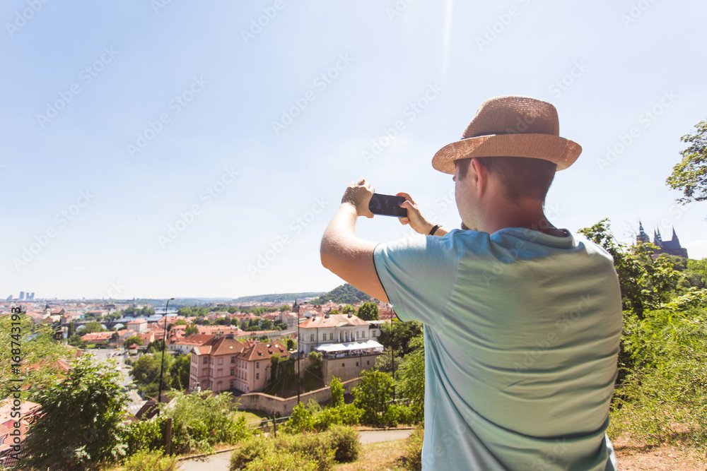 Back view of a young man tourist taking photo with smartphone in front of city