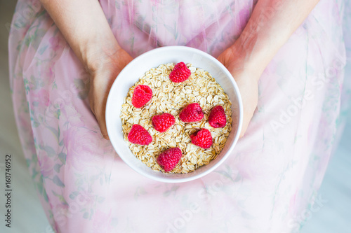 Woman's hands hold healthy and natural breakfast, oatmeal and raspberries in a bowl