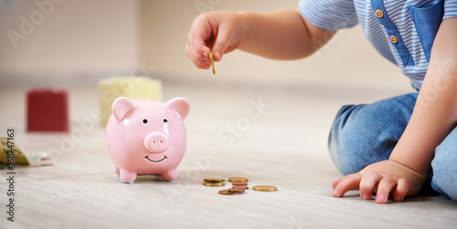 Quadro em tela two years old child sitting on the floor and putting a coin into a piggybank