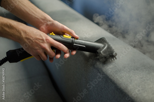 Hands cleaning a sofa with a steam cleaner