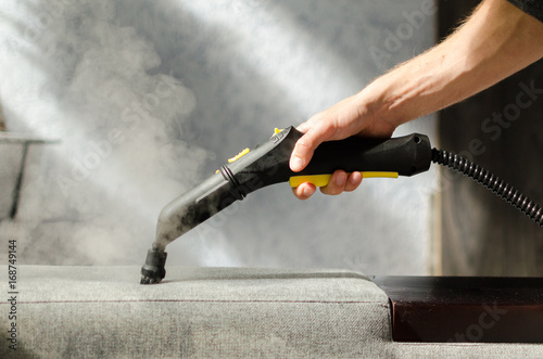 Hand cleaning a  sofa with a steam cleaner. Home cleaning concept.