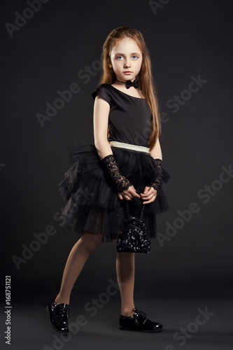 Young girl in a black dress with black bag on a black background. Girl is preparing for Halloween holiday