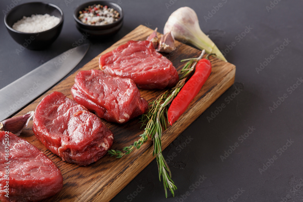 Filet mignon steaks and spices on wood at black background