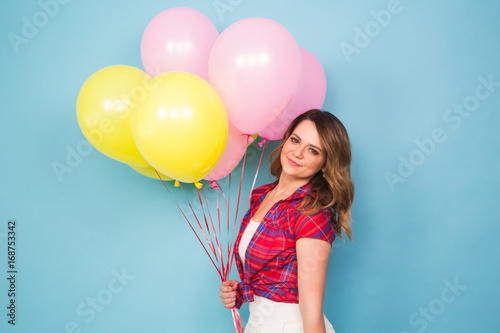 Portrait of cute girl in a studio smiling and playing with yellow and pink balloons, background with copyspace. Party, celebrate and people concept.