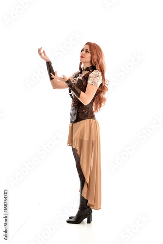 full length portrait of a red haired lady wearing steampunk inspired outfit, standing pose against a white background.