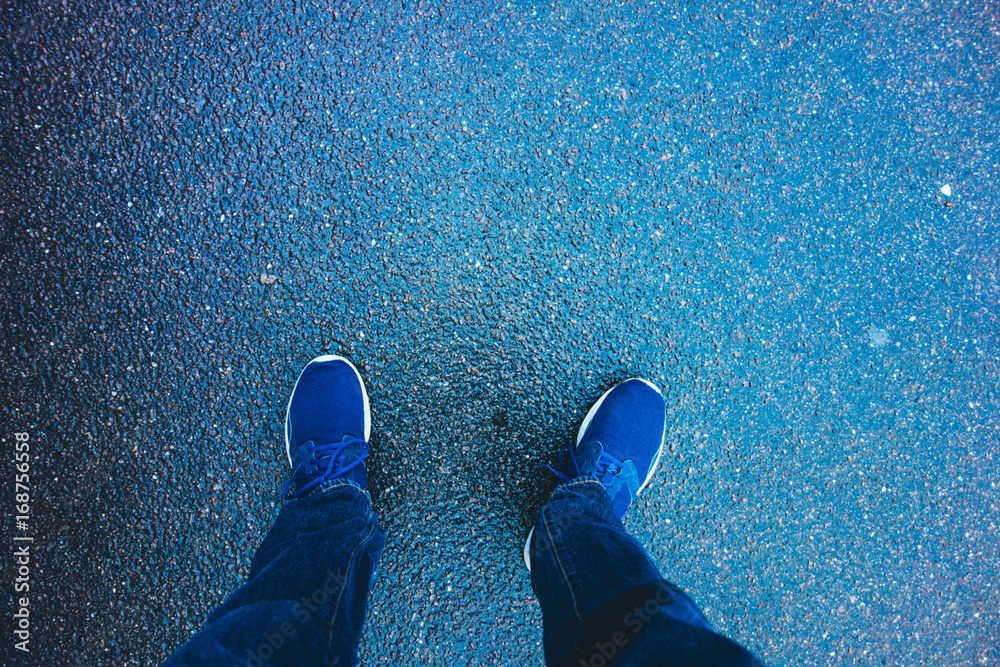 Naklejka premium man looking down to his sport shoes on blue ground