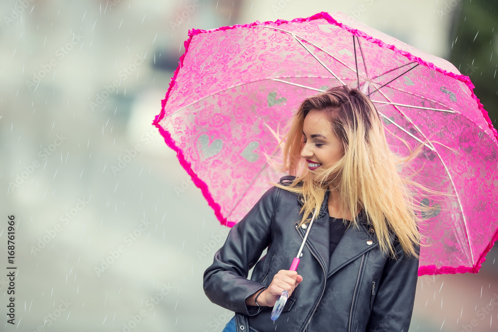 Fototapeta premium Attractive young woman with pink umbrella in the rain and strong wind. Girl with umbrella in autumn weather