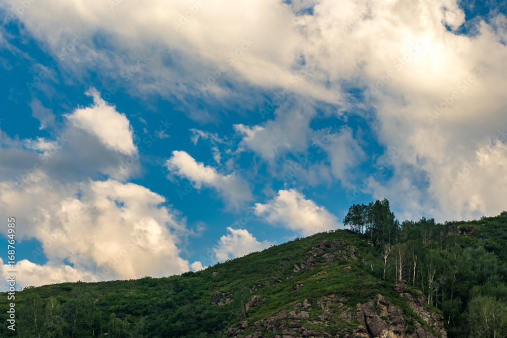A woody and rocky hill lit by bright sun rays in the summer morning, Altai Mountains, Kazakhstan A woody and rocky hill lit by bright sun rays in the summer morning, Altai Mountains, Kazakhstan