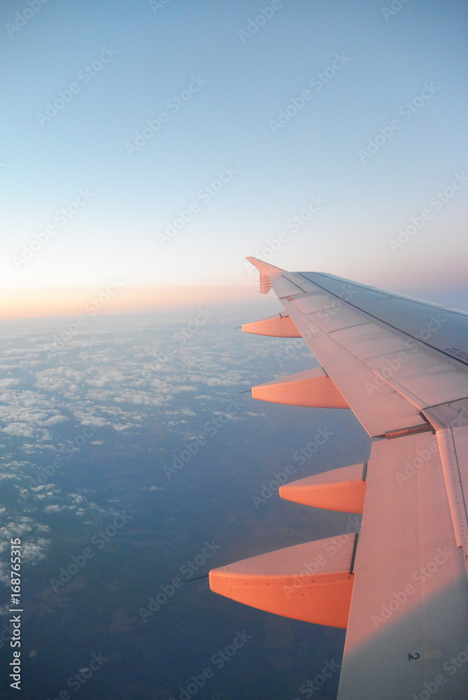 Wing of an airplane flying above the sunrise cloudy sky at morning