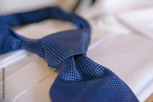 Silk blue necktie tied in a Windsor knot, resting on a white shirt, in preparation for a formal event, job interview or a wedding ceremony, or as part of office attire. 