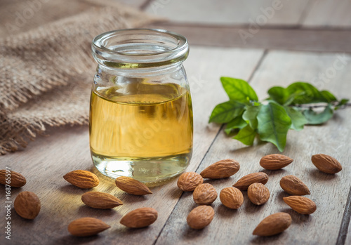 Almond oil in glass bottle and almonds on wooden table