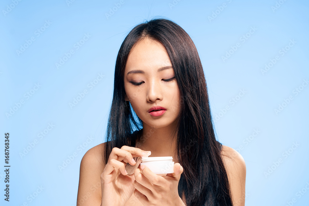 Beautiful young woman on a blue background holds a cosmetic face cream,Asian Beautiful young woman on a blue background holds a cosmetic face cream,Asian