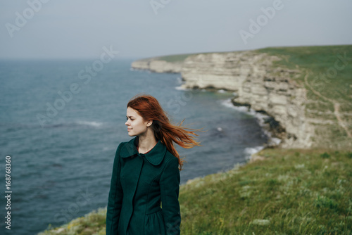 Beautiful young woman standing on a cliff of a mountain near the sea