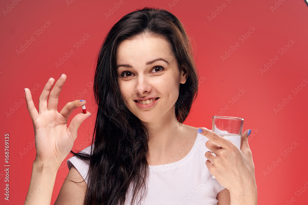 Beautiful young woman on a red background holds a pill Beautiful young woman on a red background holds a pill