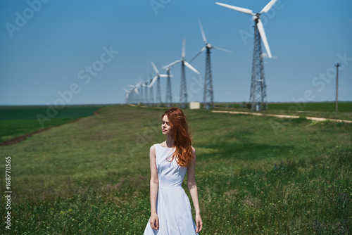 Beautiful young woman in a white dress in a field near a windmill