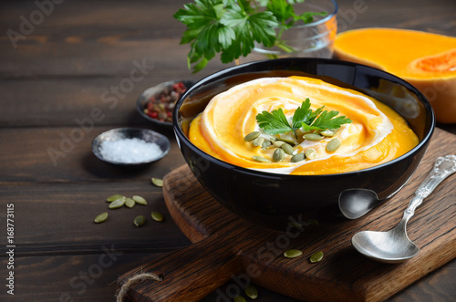 Pumpkin cream soup with cream and pumpkin seeds on wooden background, selective focus, horizontal photo