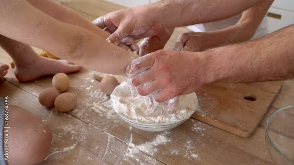 Hands of parents and the son during cooking dough. Flour on a table of the light kitchen..