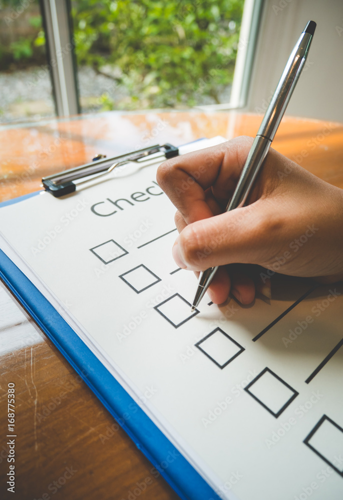 Close- up hand holding pen on check list paper and the format for ...