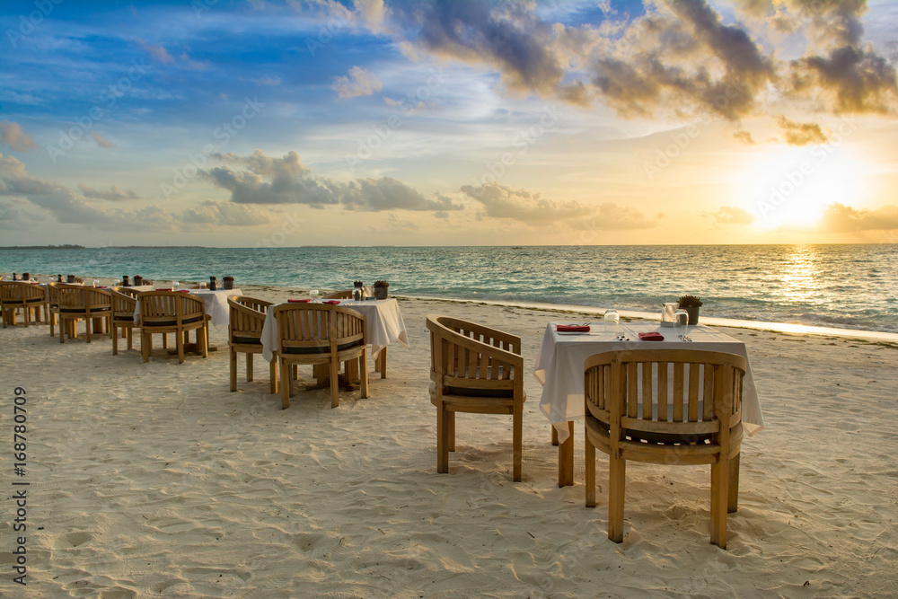 Tropical restaurant on the sandy beach. Landscape of beautiful sunset in Maldives island with colorful sky and dramatic clouds over wavy sea. Tropical restaurant on the sandy beach. Landscape of beautiful sunset in Maldives island with colorful sky and dramatic clouds over wavy sea.