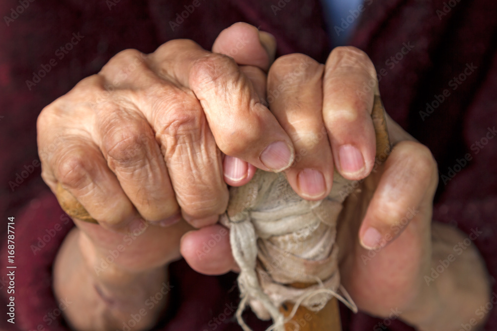 Hands of an old woman on a wooden crutch