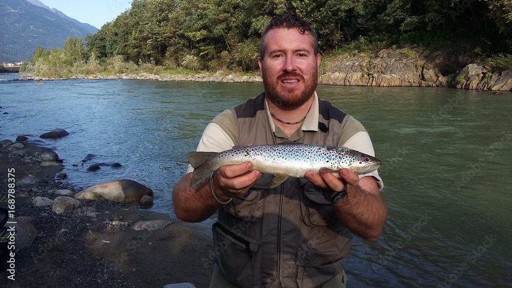 Pescatore in riva al fiume con trota fario Pescatore in riva al fiume con trota fario