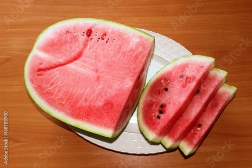 A ripe watermelon is cut and lies on a large white dish.